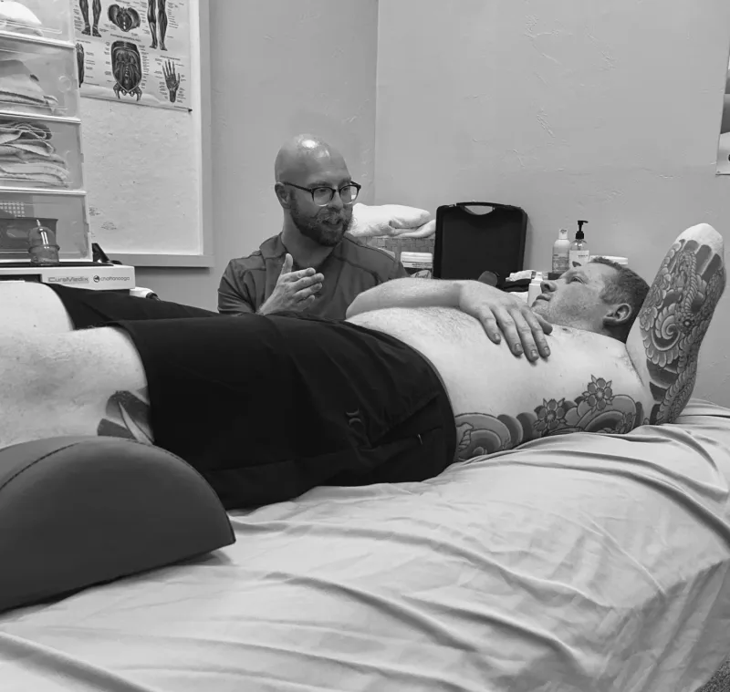 Black-and-white photo of a client on a treatment table talking with the practitioner