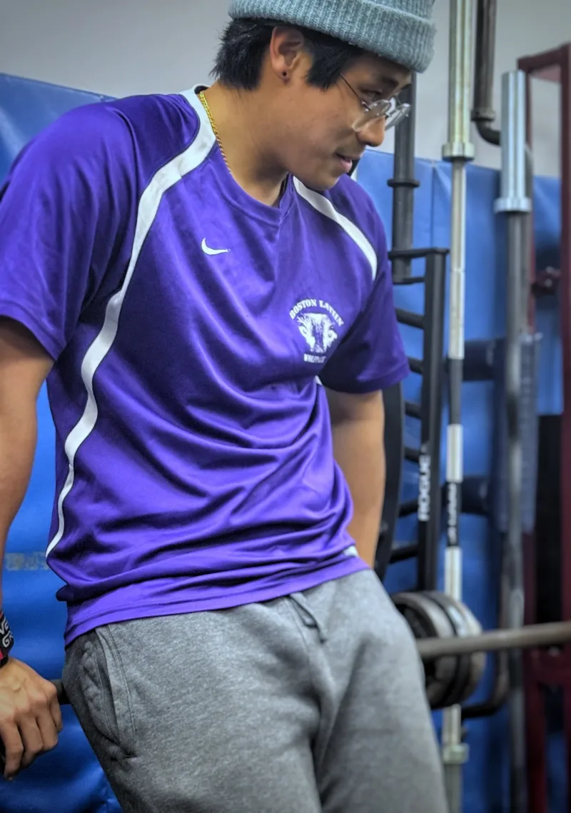 Client in a purple athletic shirt beside a barbell rack in the gym
